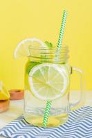 Citrus lemonade water with sliced lemon and mint, healthy and detox water drink in summer on wooden table with yellow background photo