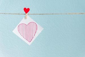 Red Valentine's love hearts pin hanging on natural cord against blue background. drawn heart on paper piece. photo