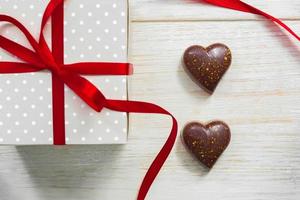 Greeting card for st valentines day. Chocolate sweets in heart shape and giftbox with red celebration ribbon on wooden background photo