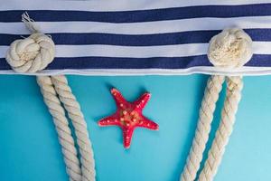 conchas marinas, estrellas de mar y bolsa azul marino con nudos de cuerda sobre fondo azul claro. concepto de vacaciones y vacaciones de verano foto