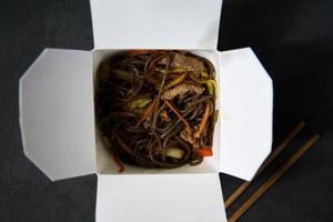 Delivery of hot lunches in boxes. Soba noodles with beef and vegetables on a black background photo