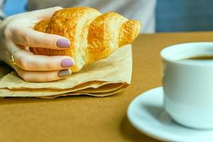 Female hands with manicure holding croissant. Breakfast in french style photo