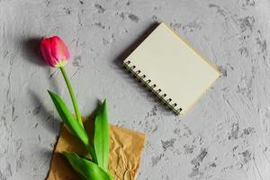 Beautiful freshly cut pink tulip and empty blank spyral note book on gray concrete background. Mock up with copy space. photo