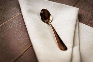 Close up of textile beige napkin and served tea spoon on wooden table. photo