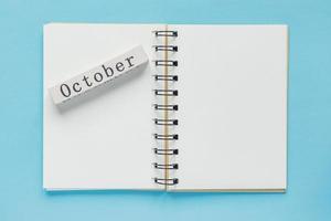 Clean spiral note book for notes and messages and october wooden calendar bar on blue background. Minimal business flat lay photo