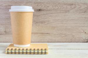 craft paper coffee cup and notebook diary with copy space on wooden table in minimalism style photo