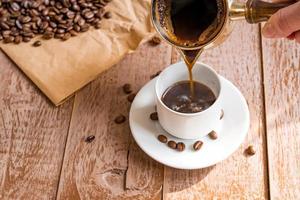 café recién hecho en cezve, cafetera tradicional turca, la mano de una mujer vierte café en una taza blanca foto