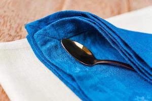 close up of cloth napkins of beige, blue colors and served tea spoon on wooden table. photo