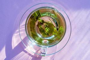 top view of transparent cup with green tea on purple background. photo