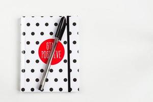 Black and white polka dot note book with red circle  on the cover and black pen on white table. top view, minimal flat lay photo