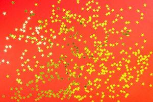Red backdrop with glitter and golden stars confetti. Festive holiday bright background photo