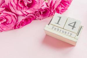 valentines day and holidays concept - close up of wooden calendar with 14th february date,  and pink roses with on pink background photo