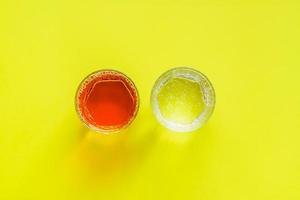 top view of transparent glasses with apple juice and sparkling water on yellow background photo