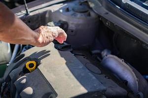 mecánico revisando y arreglando un tapón de llenado de aceite de un automóvil roto en un automóvil en la carretera. foto