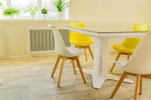 Modern dining room designed in scandi style. Glass table and yellow and white chairs