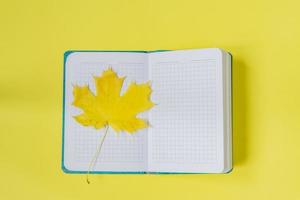 Blank open notebook with maple leaf  on yellow background. Empty diary and autumn concept photo