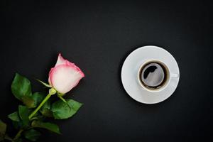 Cup of black coffee and pink rose on black background, Top view, copy space. photo