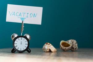 Alarm clock and banner with handwritten phrase vacation on wooden table. Vacation concept. photo