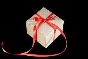 Beige polka dot gift box with red ribbon bow on black background with copy space. photo