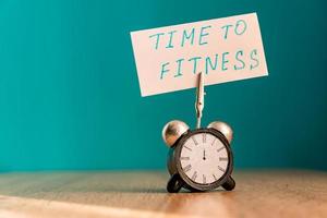 Alarm clock and banner with handwritten phrase time to fitness on wooden table. Time management concept. photo