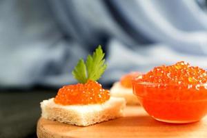 delicioso caviar rojo en pan de trigo servido con perejil en un escritorio de madera. foto