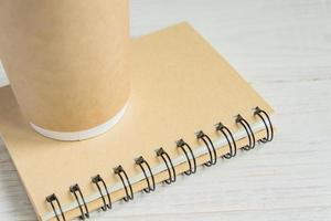 craft paper coffee cup and notebook diary with copy space on wooden background photo