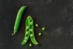 telón de fondo vegetal con espacio de copia para sus proyectos. Cerca de guisantes verdes maduros frescos sobre fondo negro foto