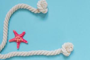 Red starfish and knot rope on light blue background with copy space. summer holiday and vacation concept photo