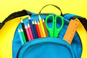 Blue Backpack with different colorful stationery on yellow background. Back to school photo