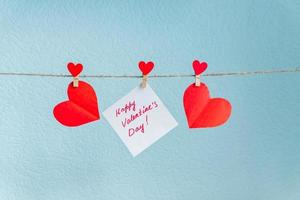 alfileres de corazones de amor de san valentín rojo colgando de un cordón natural sobre fondo azul. foto