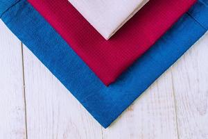 close up of cloth napkins of beige, blue and burgundy colors on rustic white wooden table. Shallow depth of field. photo