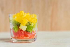 Diet Fresh tasty mix fruit salad in a glass jar on rustic wooden background. Chopped juicy oranges, kiwi and grapefruits. photo