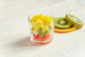 Diet Fresh tasty mix fruit salad in a glass jar on wooden table. Chopped juicy oranges, kiwi and grapefruits. photo