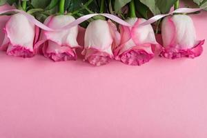 rosas florecientes rosadas y cinta sobre fondo rosa pastel. marco floral romántico. copie el espacio foto