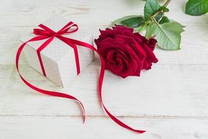 Beige polka dot gift box with red ribbon bow and bautiful red roses on wooden background. Greeting card for holiday. photo