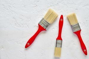 three paintbrushes with red handles on freshly made concrete background. Repairing concept. Top view with copy space photo