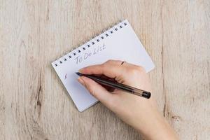 mano de mujer joven abrió páginas de cuaderno con bolígrafo negro sobre una mesa de madera. para hacer la lista de escritura a mano. foto