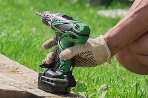 electric screwdriver in males hand in textile glove outdoors. Man working with a hand tool on the backyard. photo