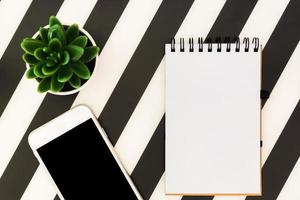 Stylish minimalistic workspace with notebook, mobile phone and succulent on striped black and white background. Flat lay style Top view. photo