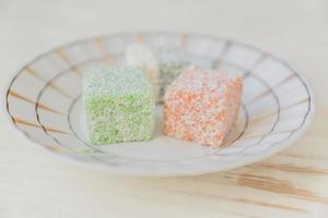 Traditional turkish delight on a plate on white wooden background. Assorted Oriental sweets. photo