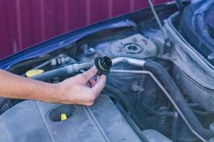 mecánico revisando y arreglando un tapón de llenado de aceite de un automóvil roto en un automóvil en la carretera. foto