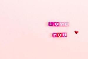 Love you  inscription made of colorful cube beads with letters. Festive pink background concept with copy space photo
