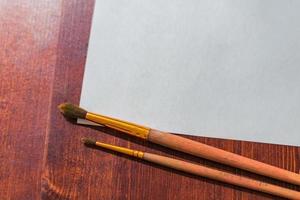 two paint brushes and clear sheet of paper on wooden table. creative mockup. photo