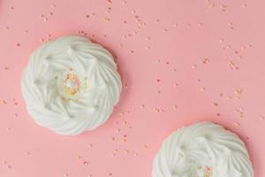 homemade white air meringues and confectionery decorations on pink background photo