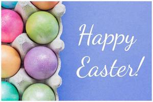 Multicolored easter eggs in a box on blue background, Top view. Greeting card Happy Easter photo