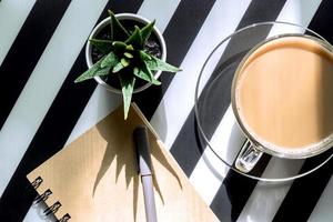 Stylish minimalistic workspace with notebook, pen, cup of coffee and succulent on striped black and white background. Flat lay style Top view. photo