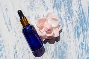 Serum or cosmetic liquid, oil on a wooden blue background with rose flower. Concept for natural cosmetics, not tested on animals. Natural ingredients photo