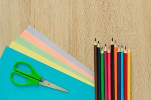 Top view of multicolored paper, pencils and scisors on wooden table. Top view.  Arrangement for creative work or craft. photo