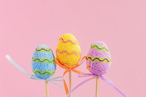 Easter purple, yellow and blue decorated eggs stand on a wooden sticks on pink background. Minimal easter concept. Happy Easter card with copy space for text. photo