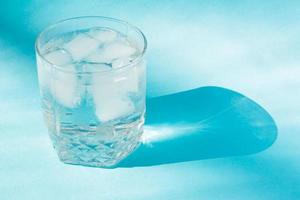 Close up of pure water with ice in transparent glass and sun glare on blue background. photo